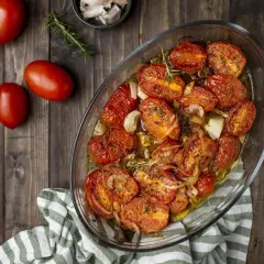 Pomodori gratinati al forno, dorati e succosi, con cipolle e rosmarino in una teglia di vetro su un tavolo di legno.