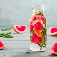 Erfrischendes Detox Wasser mit Grapefruit und Rosmarin in einer Glasflasche, umgeben von frischen Fruchtscheiben und Kräuterzweigen.
