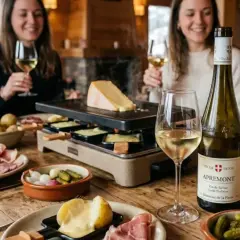 Un groupe d'amis savoure une raclette, accompagnée d'un vin rouge de Savoie. Les pommes de terre, charcuteries et cornichons sont prêts à être dégustés.