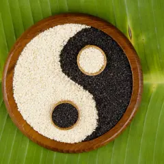 Simboli yin e yang di semi di sesamo bianchi e neri, disposti su una foglia verde.