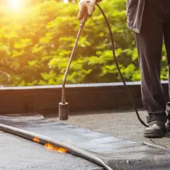 Pracownik z palnikiem gazowym uszczelnia papę na dachu. Dobór odpowiednich szpilek do murłaty jest kluczowy dla trwałości pokrycia.
