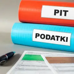 Dwa segregatory: czerwony z napisem "PIT" i niebieski z napisem "PODATKI". Obok formularze podatkowe i długopis. Ulga dla młodych w zasięgu ręki.