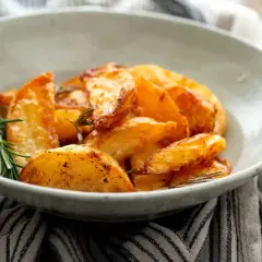 Patatas al horno en rodajas, doradas y crujientes, servidas en un cuenco con romero fresco.