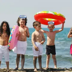Piątka dzieci cieszy się wakacjami, gotowa na zabawy na plaży. Wśród nich są koła ratunkowe i wiaderko.