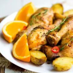 Pyszne udka pieczone z ziemniakami i warzywami, ozdobione pomarańczą i ziołami.