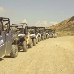 Una fila de vehículos todoterreno espera en un camino de tierra, listos para una aventura por el desierto, como si fueran un puente de todos los santos hacia lo desconocido.