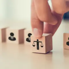 Dłoń układa kostkę z wagą sprawiedliwości obok kostek z ludzikami. To symbol tego, co daje członkostwo w partii: równość i reprezentację.