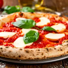 Eine neapolitanische Pizza Margherita mit frischem Basilikum und Mozzarella auf einem Holztisch.