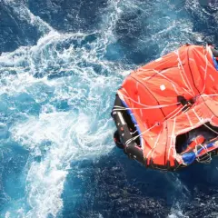 Una zattera di salvataggio arancione galleggia in un mare agitato. Il suo significato è speranza e sopravvivenza.