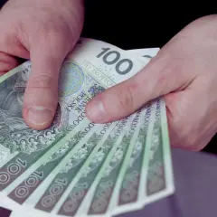 Dłonie trzymają stos banknotów 100 zł. To może być wypłata, premia lub kwota bliska minimalna brutto.