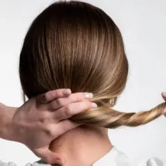 Manos trenzando el cabello rubio para crear peinados para dormir que mantengan el pelo bonito.