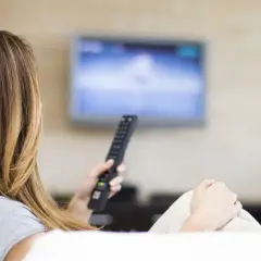Kobieta z pilotem w ręku ogląda telewizję, ciesząc się swoim abonamentem radiowo-telewizyjnym.