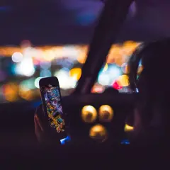 Hand hält Handy mit Stadtansicht, während sie geblitzt wird. Bokeh-Lichter im Hintergrund.