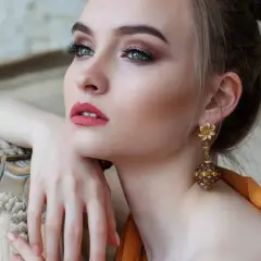 Donna con elegante trucco semplice, labbra rosse e orecchini pendenti dorati.