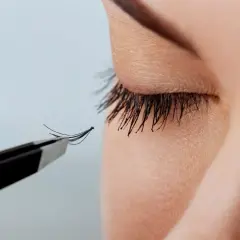 Pęseta trzyma kępkę sztucznych rzęs przy oku z naturalnymi rzęsami.