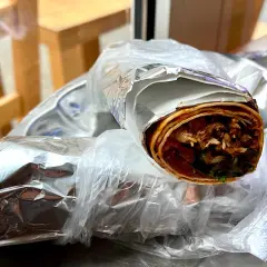 Dwa zawinięte w folię aluminiową i folię spożywczą tureckie wrapy z mięsem i warzywami na talerzu.