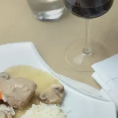 Un verre de vin rouge accompagne une blanquette de veau savoureuse avec riz et champignons.