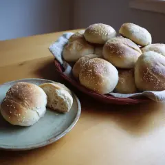 Färska frallor med sesamfrön, redo att avnjutas. En korg full av nybakade godsaker och en tallrik med en delad fralla. Perfekt för frukost eller fika.