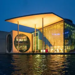 Nowoczesne muzeum sztuki w Berlinie, z charakterystycznym okrągłym oknem i przeszkloną fasadą, odbija się w wodzie.
