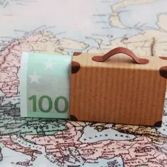 Miniaturowa walizka i banknot 100 euro na tle mapy Europy.