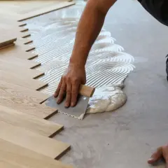 A worker applies adhesive to the subfloor for installing wood snap in flooring.