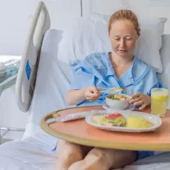 Kobieta w szpitalnym łóżku je posiłek. Zastanawia się, ile po cesarce można jeść, by szybko wrócić do formy.