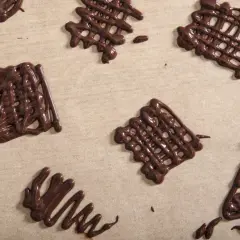 Czekoladowe ozdoby na tort w kształcie siatek i choinki, wykonane na papierze do pieczenia.