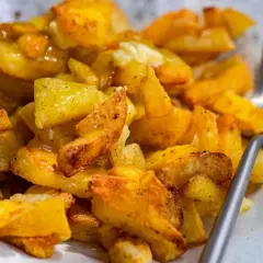 Un plato de papas al horno crujientes, doradas y sazonadas, listas para disfrutar con un tenedor.