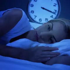 Kobieta leży w łóżku, patrząc w sufit. Obok niej budzik pokazuje późną noc. Czy zastanawia się, lorafen na co pomoże jej zasnąć?
