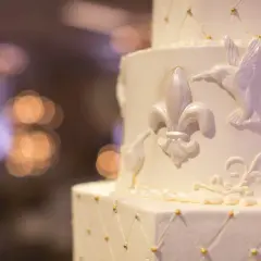 Biały tort weselny z ozdobami z masy cukrowej: lilie, kolibry i złote kuleczki.
