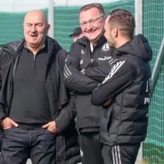 Stanisław Czerczesow w otoczeniu współpracowników, uśmiechnięci na tle zielonej siatki.