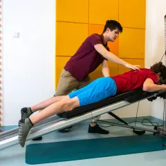 Fizjoterapeuta pomaga pacjentowi w ćwiczeniach na ławce rehabilitacyjnej. Skupiają się na rehabilitacji ortopedycznej, by odzyskać sprawność.