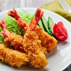 Crispy, golden japanese fried shrimp served on a bed of shredded cabbage with cucumber and tomato slices.