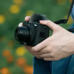 Dłonie trzymają aparat Canon z mikrofonem, gotowe do uchwycenia pięknych chwil. Aparat fotograficzny służy do tworzenia wspomnień.