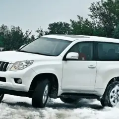 Toyota Land Cruiser 3.0 D4D 163 CV ficha técnica: un blanco todoterreno navega por nieve y agua, demostrando su potencia.