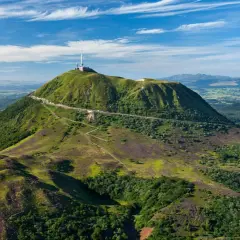 Vue aérienne du Puy de Dôme, un des volcans d'Auvergne, avec sa route en lacets et son antenne. Paysage verdoyant sous un ciel bleu.