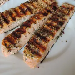 Trzy grillowane filety łososia, przyprawione ziołami, wyglądają apetycznie. Idealna marynata do lososia sprawia, że ryba jest soczysta i aromatyczna.