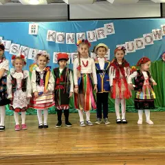 Dzieci w pięknych strojach ludowych prezentują się na scenie podczas konkursu.