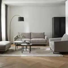 Nowoczesny salon z szarymi meblami i dywanem. W tle czarna szafa i zasłony w odcieniach szarości.