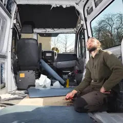 Uomo lavora all'isolamento di un'auto camperizzata. Materiali sparsi, sedili rimossi, pronto per la trasformazione.