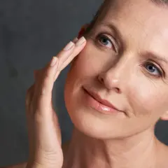 Une femme touche délicatement son visage, révélant une peau mature. La question "peau mature à partir de quel âge" se pose naturellement.