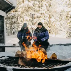 Couple réchauffé au feu de bois en Laponie. Idéal pour savoir quand partir en Laponie pour une expérience hivernale magique.