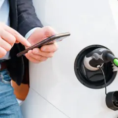 Mężczyzna sprawdza na telefonie, jak rozliczyć ładowanie samochodu elektrycznego w domu. Zielony kabel podłączony do pojazdu.