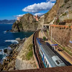 Zug fährt entlang der Küste von Cinque Terre. Bunte Häuser kleben an steilen Felsen über dem blauen Meer.