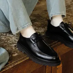 Paire de chaussures noires en cuir synthétique, lacées, avec une semelle épaisse. Parfaites avec un jean décontracté.