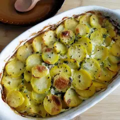 Pyszna zapiekanka ziemniaczana z kurczakiem, posypana ziołami, w białym naczyniu żaroodpornym.