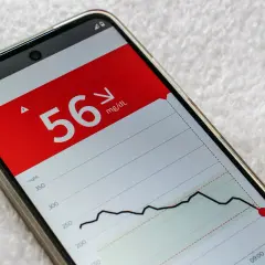 Telefon z aplikacją pokazującą niski poziom cukru 56 mg/dL i wykres glikemii.