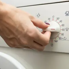 Main d'une personne réglant le bouton d'une machine à laver pour le lavage de vêtements.