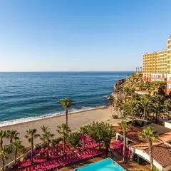 Hotel con piscina y tumbonas rosas junto a la playa de aguadulce roquetas de mar, con el mar azul de fondo.