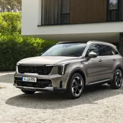 SUV Kia Sorento color sabbia, un esempio delle migliori auto benzina, parcheggiata su ghiaia davanti a una casa moderna.